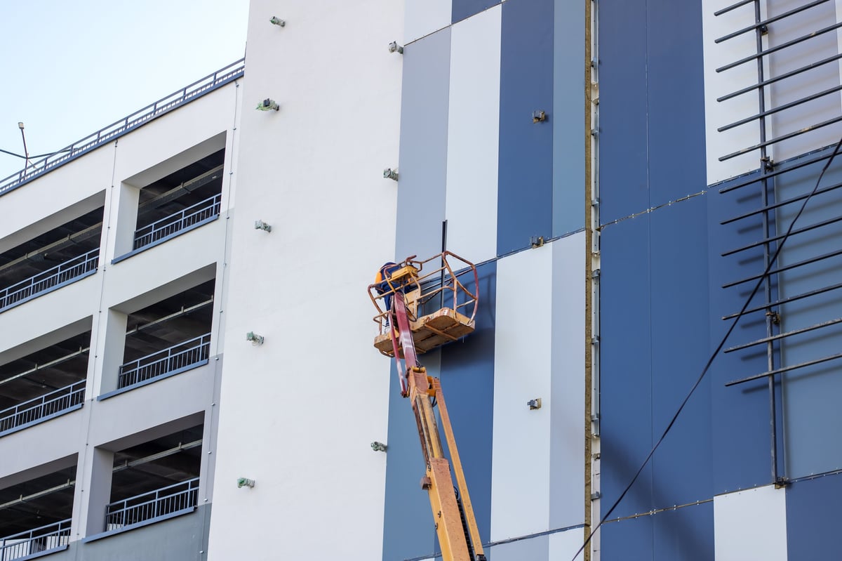A man is seen inside a lift painting the side of a building