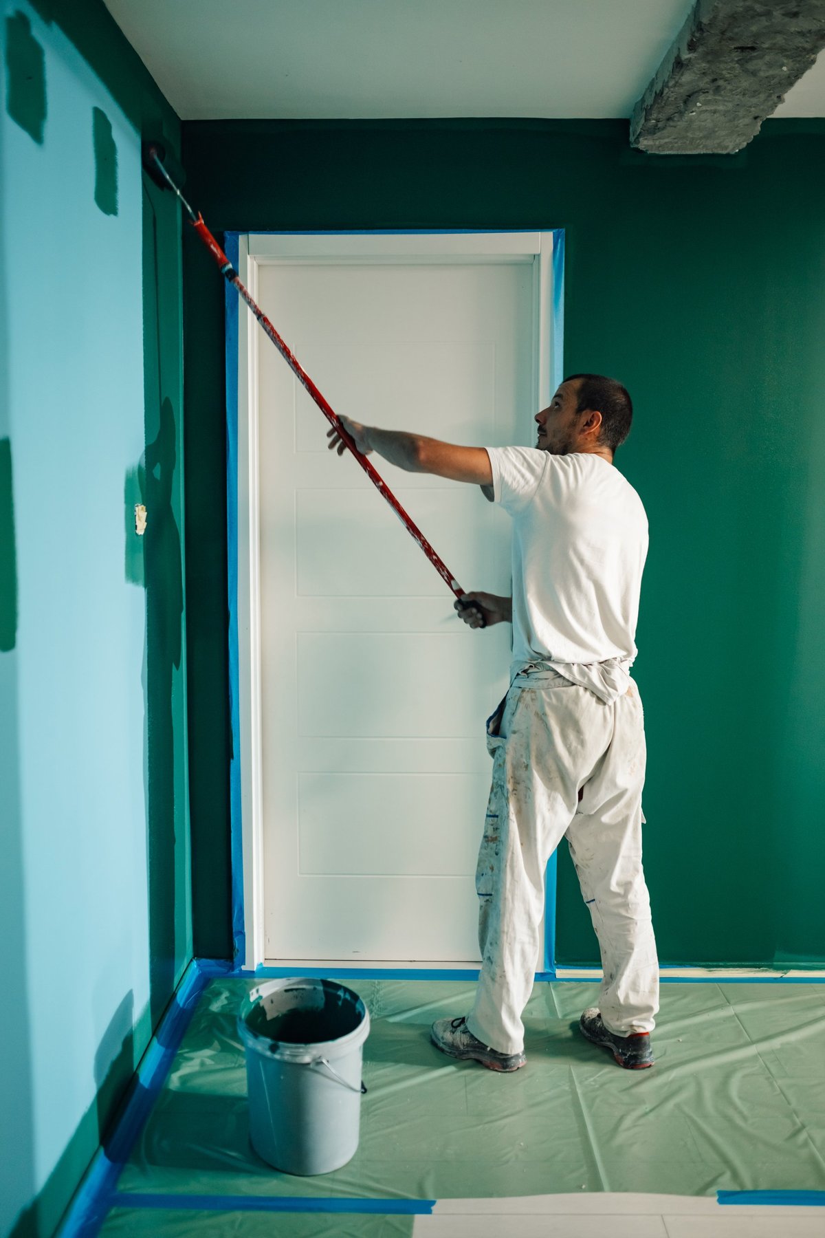 Painter applying vibrant green paint on a wall, transforming the space during a home renovation